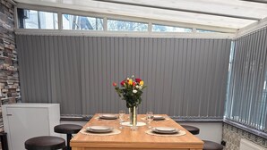 A dining area with a wooden table, four black bar stools, and a vase of flowers. - Argyleluxe (Worsley)