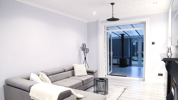 A modern living room with a grey sectional sofa, a small black side table, and a white throw blanket. - Argyleluxe (Worsley)