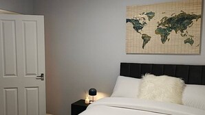 A neatly made bed with a white pillow and a rolled towel, a world map on the wall, and a closed door. - Argyleluxe (Worsley)
