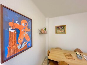 A dining area with a wooden table, chairs, a framed painting, and a shelf with decorative items. - Refuge Douillet - Esprit Alsacien -Ballon d'Alsace (Masevaux-Niederbruck)