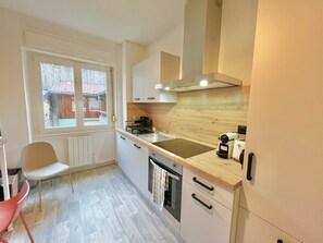 A compact kitchen with a window, a stove, a sink, and a small dining area. - Refuge Douillet - Esprit Alsacien -Ballon d'Alsace (Masevaux-Niederbruck)