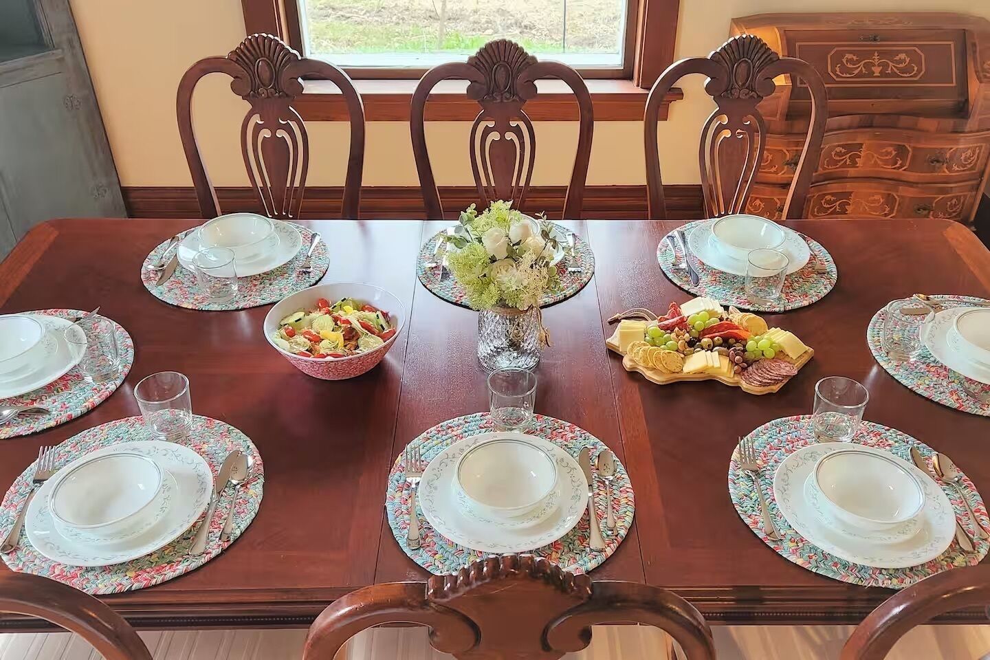 Une table à manger dressée pour six personnes, avec des sets de table à motifs floraux, un centre de table et une variété de plats.