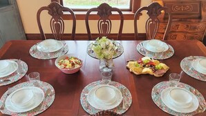 A dining table set for six with floral placemats, a centerpiece, and a variety of food items.