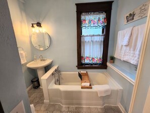 A bathroom with a bathtub, sink, and window with floral curtains.