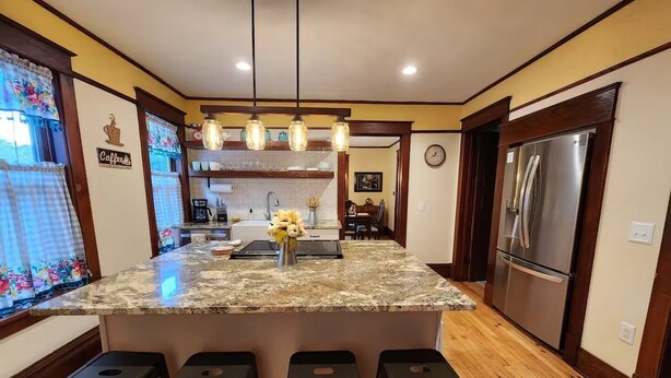 A kitchen with a granite island, bar stools, a refrigerator, and a coffee sign.