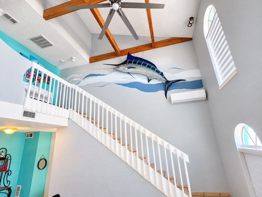 A staircase with a ceiling fan, a wall mural of a fish, and a window with blinds.