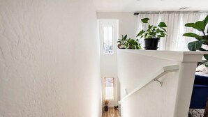 Una escalera con paredes blancas y peldaños de madera que lleva a un descansillo con ventana y plantas en macetas.