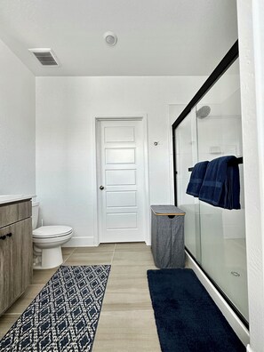 A modern bathroom with a toilet, a sink, a glass shower enclosure, and a patterned rug. - Clovis Retreat - Modern 2BR Near Parks, Pool (Clovis)