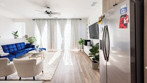 Una sala de estar moderna con un sofá azul, un sillón blanco, una mesa de centro y un ventilador de techo.