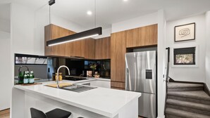 A modern kitchen with a central island, stainless steel appliances, and a wooden accent wall. - Alpine Vision Chalet (Dinner Plain)