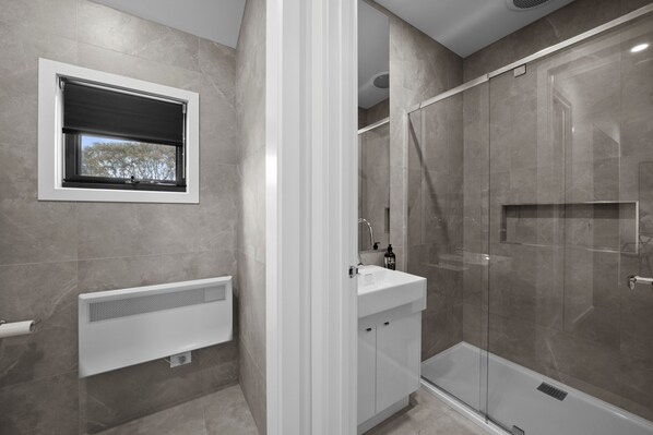 A modern bathroom with a built-in window, a white sink, and a glass-enclosed shower. - Alpine Vision Chalet (Dinner Plain)