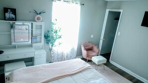 Ein Schlafzimmer mit Bett, Schreibtisch, Stuhl, Pflanze und einer Tür.