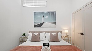 A neatly made bed with a rolled towel, a painting of a lighthouse, and a bedside table with a lamp. - 1 King Loft W/Parking + Laundry I Oak Lawn + DT (Dallas)