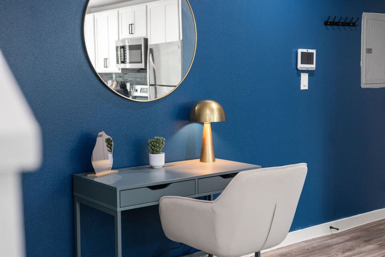Een moderne kamer met een blauwe wand, een ronde spiegel, een bureau met een lamp en een stoel.