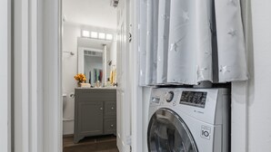 Een wasserette met een wasmachine, een spiegel en een wastafelmeubel met een wastafel en handdoekhouder.