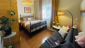 A bedroom with a bed, a bedside table, a lamp, a plant, and a window with curtains. - Enjoyable 2-bedroom house in lovely Saanich Core neighborhood (Saanich Core)