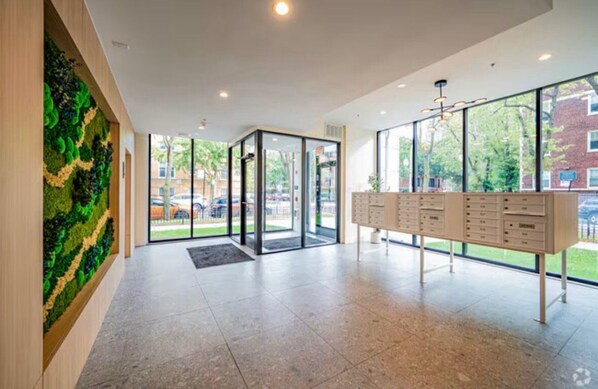 A modern lobby with a glass door entrance, a green wall feature, and a reception desk with multiple drawers.