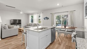 Et moderne køkken med en central ø, et spiseområde med bord og stole, en sofa og et fjernsyn i en stue.