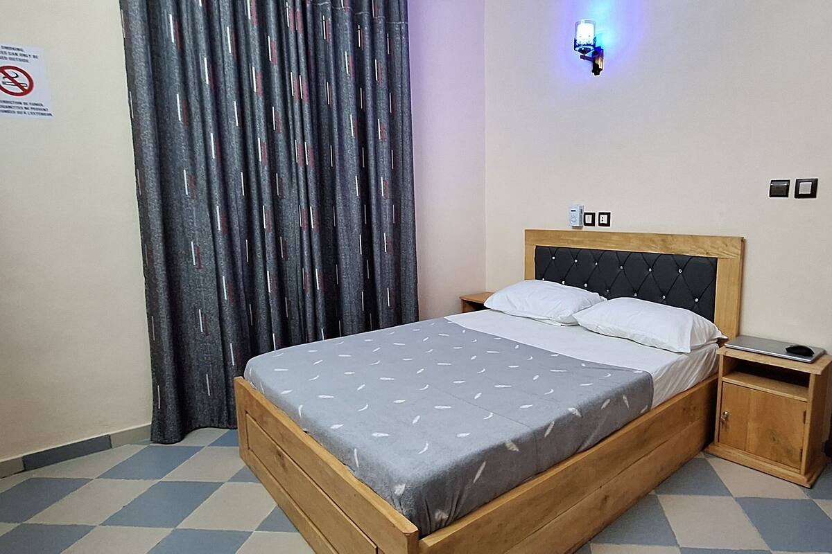 Een slaapkamer met een houten bed, een nachtkastje, een wandlamp en een deur.