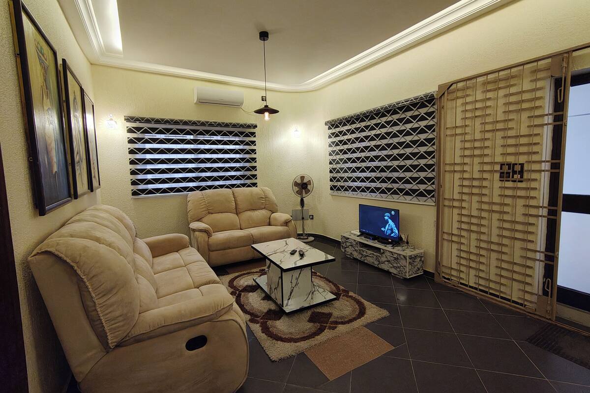 Een woonkamer met beige banken, een televisie op een dressoir en een raambekleding met dessin.