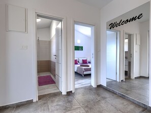 Un pasillo moderno de hotel con un cartel de 'Welcome', un baño a la vista y un dormitorio con cama y almohadas.
