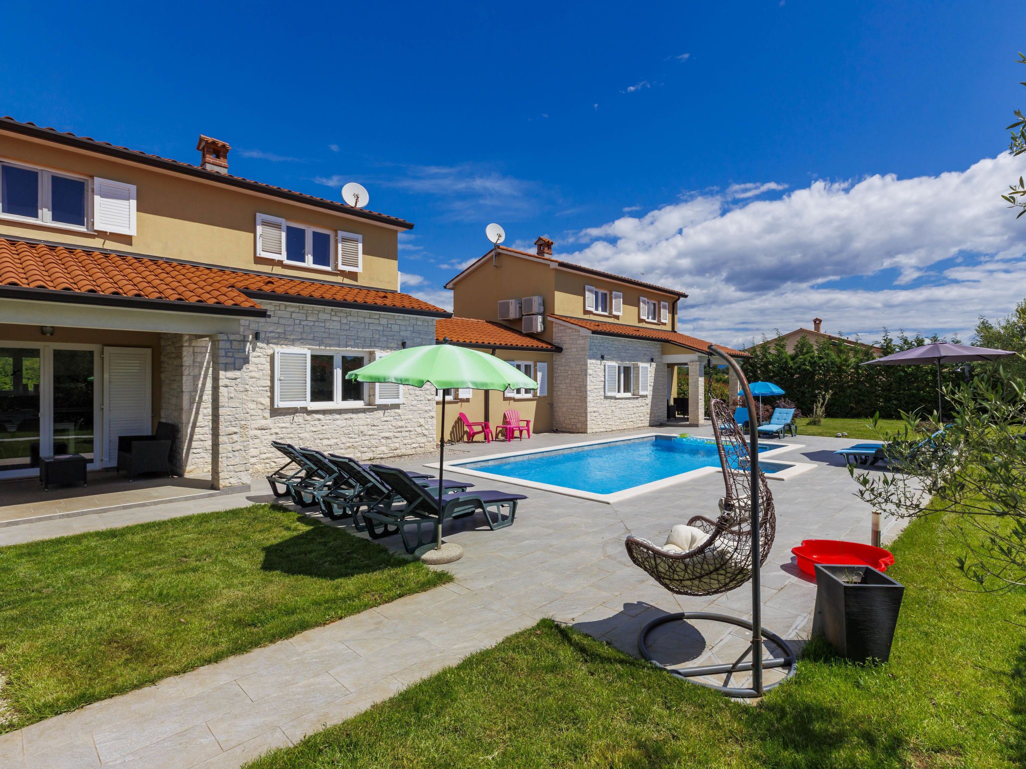 A two-story house with a swimming pool, outdoor seating, and a hanging chair.