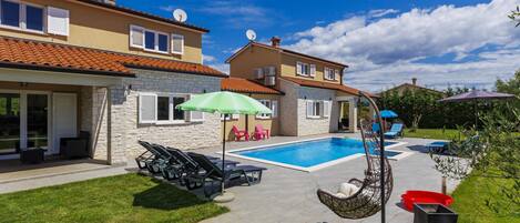A two-story house with a swimming pool, outdoor seating, and a hanging chair.