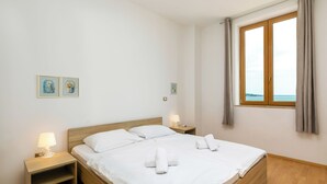 Un lit bien fait, avec du linge de lit et des serviettes blanches, une table de chevet avec une lampe et une fenêtre avec des rideaux.