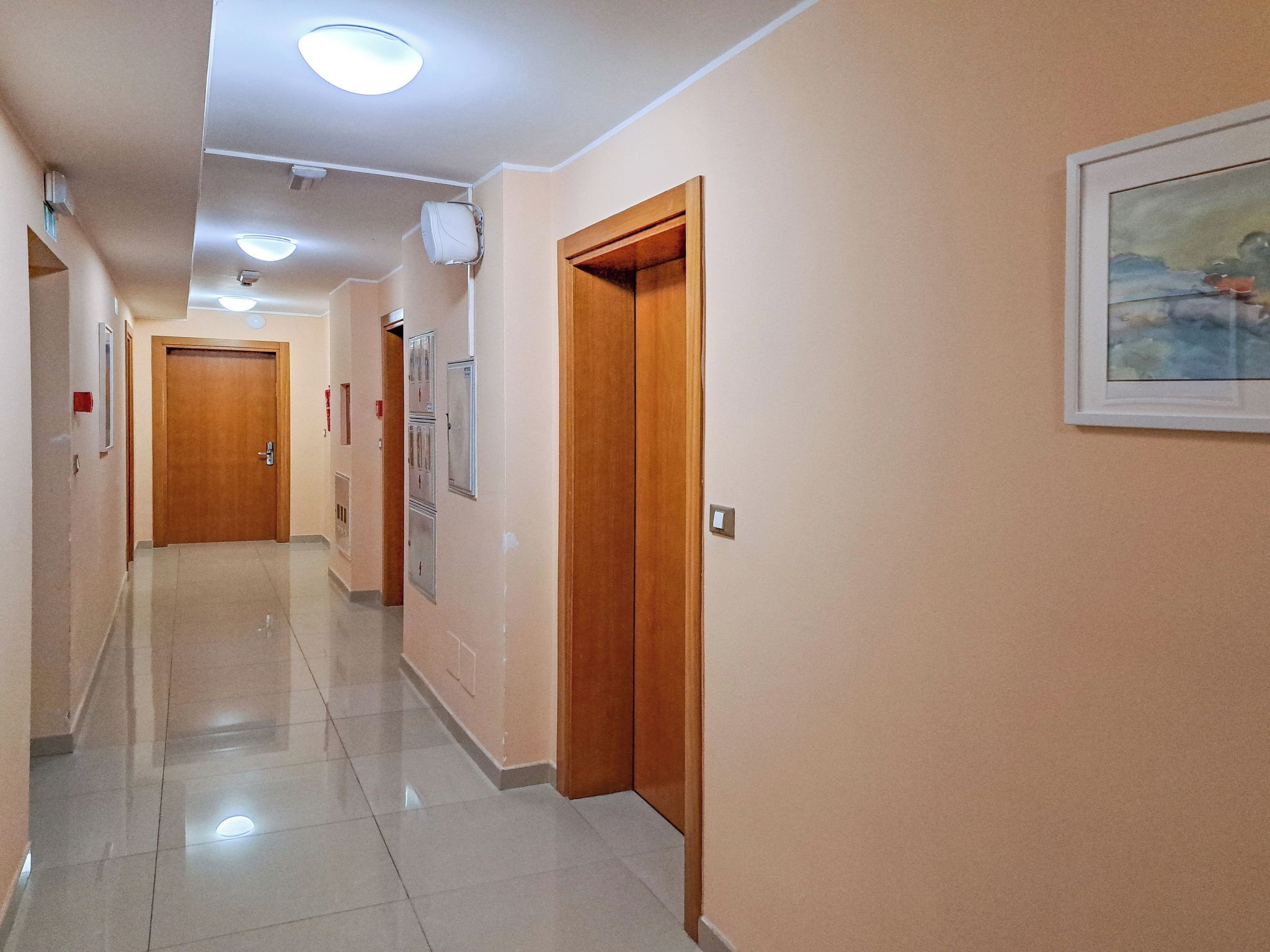 A hallway with wooden doors, tiled floors, and recessed lighting.