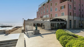 Un hôtel à la façade rose, doté d’un espace extérieur aménagé et couvert, et offrant une vue sur la mer.