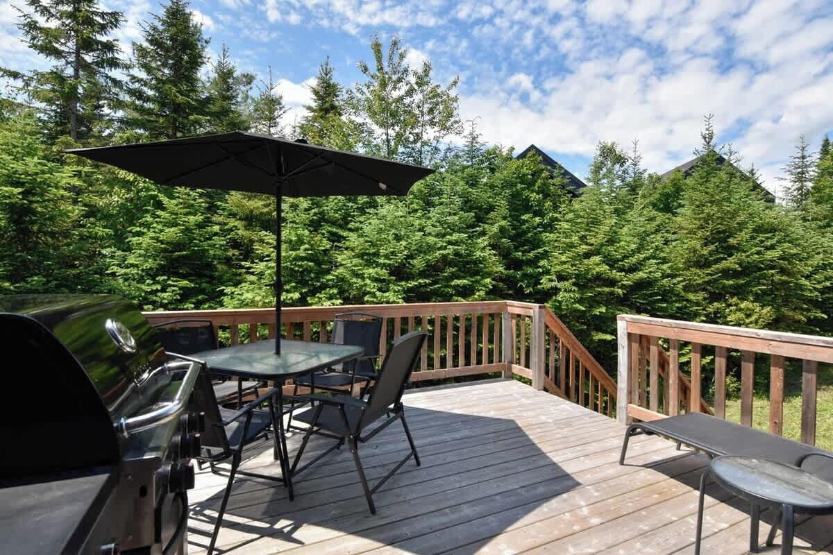 Une terrasse en bois avec un barbecue, une table, des chaises et un parasol.