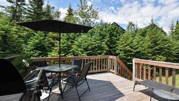 Une terrasse en bois avec un barbecue, une table, des chaises et un parasol.