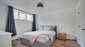 Un dormitorio con cama, mesita de noche y ventana con cortinas.