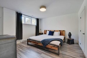 Un dormitorio moderno con estructura de cama de madera, ropa de cama blanca y una mesita de noche con un florero.