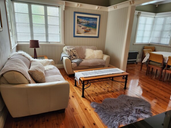A cozy living room with a sofa, a coffee table, and a painting on the wall. - The Heights! Comfortable, cosy Queenslander cottage with a retro vibe. (Wavell Heights)