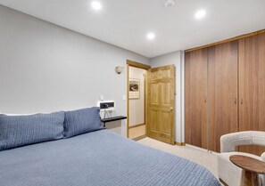 A bedroom with a large bed, a wooden wardrobe, a small table, and a chair.