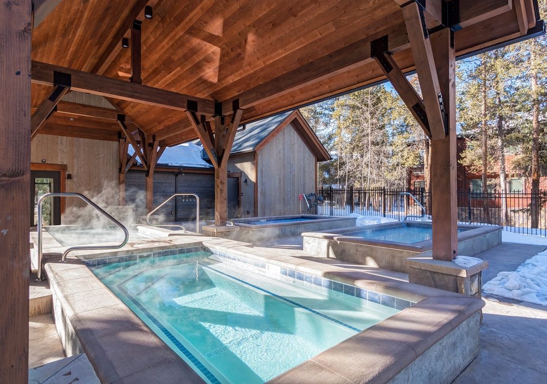 A hot tub area with a wooden pergola overhead, a pool, and a sauna.