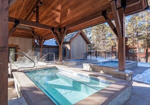 A hot tub area with a wooden pergola overhead, a pool, and a sauna.