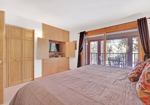 Una camera da letto con un letto grande, un armadio in legno, TV a incasso e un balcone con mobili da esterno.