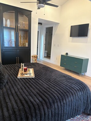 A bedroom with a large bed, a dark-colored wardrobe, a green dresser, a ceiling fan, and a television mounted on the wall.