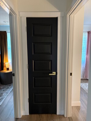 A black door with a modern handle, white trim, and a light switch on the wall.