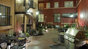 Eine Terrassenanlage im Freien mit Grill, Sitzgelegenheiten und einer Treppe, die zu einer erhöhten Ebene führt.