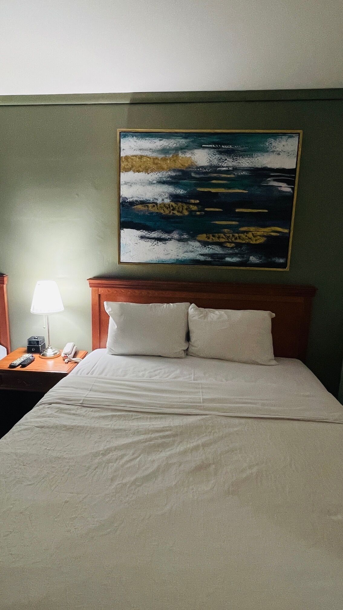 A hotel room with a bed, a nightstand, a lamp, and a painting on the wall.