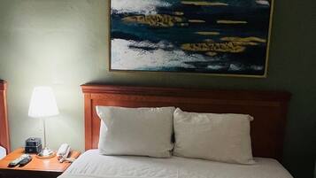 A hotel room with a bed, a nightstand, a lamp, and a painting on the wall.