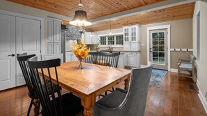 Une cuisine spacieuse avec un plafond en bois, des armoires blanches et un coin repas comprenant une table et des chaises en bois.