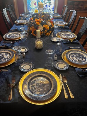 A dining table set with blue and gold plates, silverware, and a centerpiece with flowers and candles.