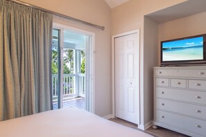 Een slaapkamer met een bed, een televisie op een dressoir, een glazen schuifdeur en uitzicht op een strand.