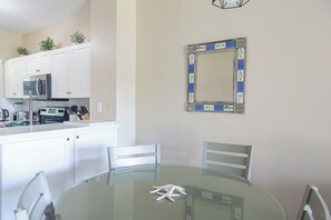 A modern kitchen with white cabinets, a microwave, and a dining area with a glass table and chairs. - Blue House Getaway - Waterfront Villa in Duck Key (Duck Key)