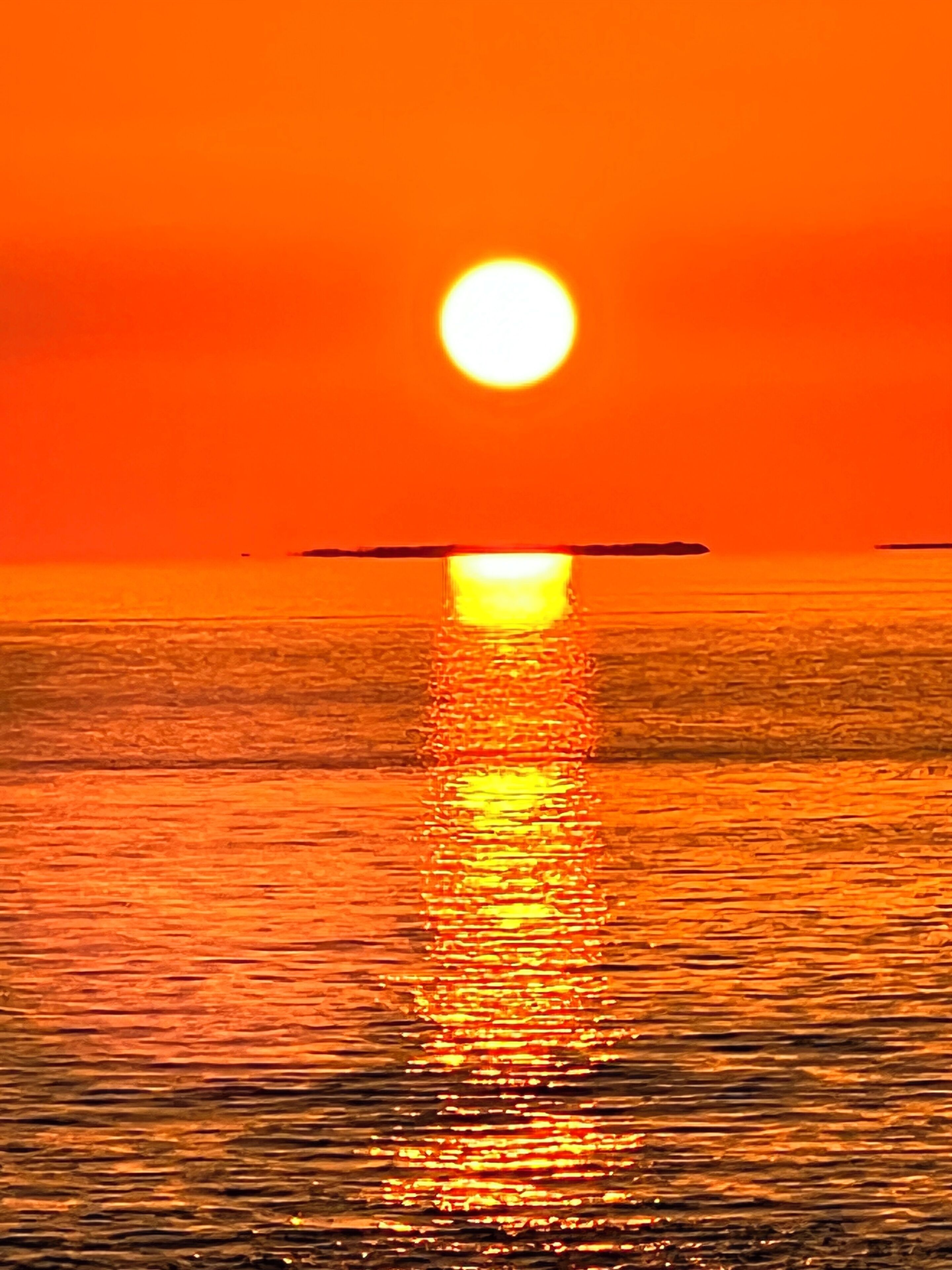 Un atardecer sobre un cuerpo de agua tranquilo, con un reflejo claro del sol.