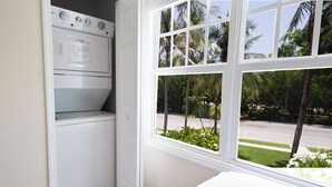 Une buanderie équipée d’un lave-linge et d’un sèche-linge intégrés, une fenêtre donnant sur des palmiers et une rue.